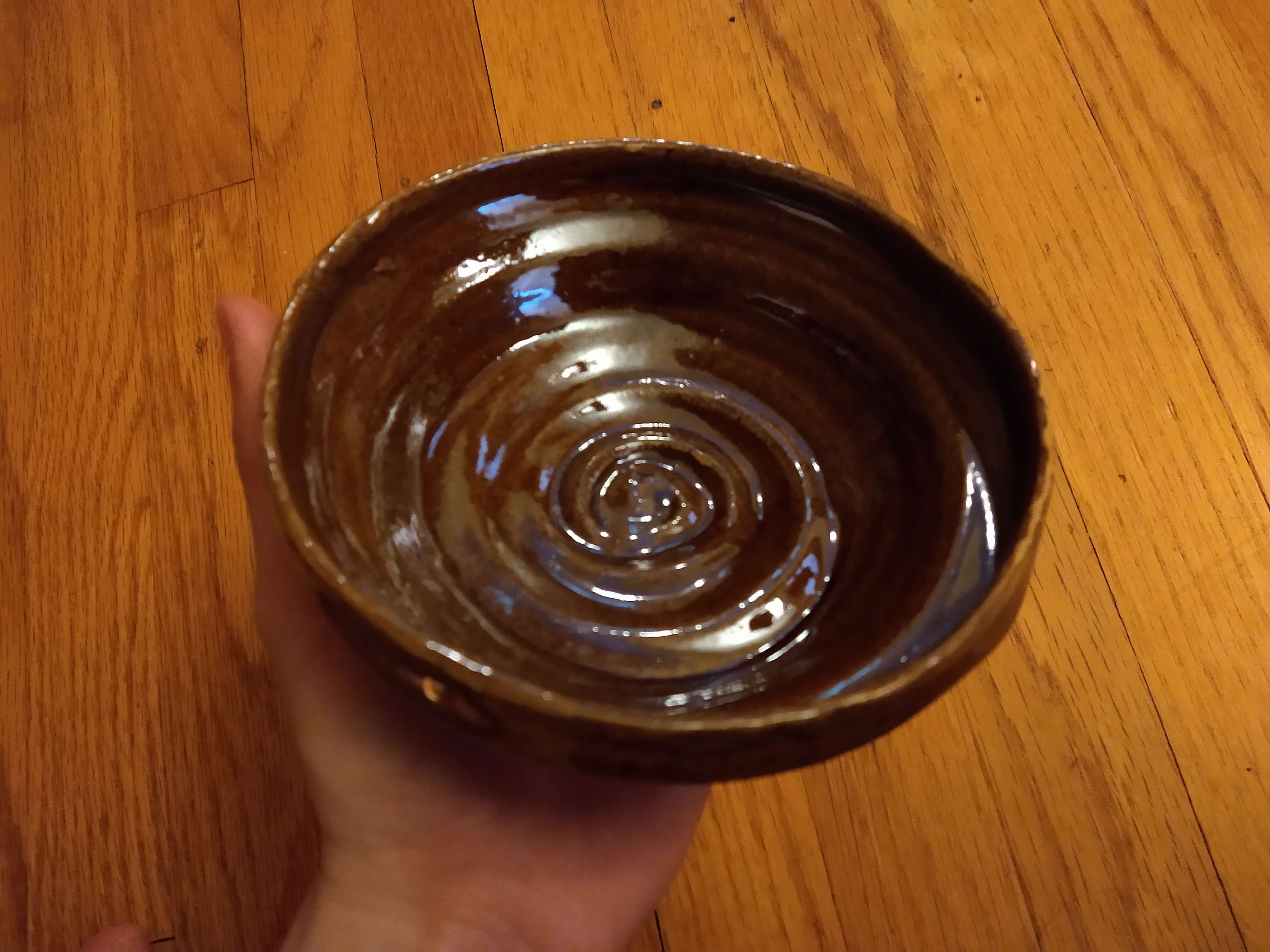 A wide, shallow brown bowl with a spiral groove in it that has a rose-like pattern.